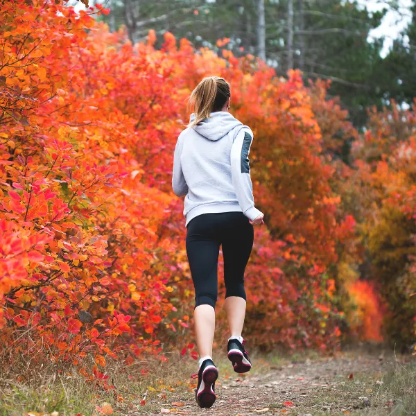 Frau joggt auf einem herbstlichen Waldweg – neue Energie mit dem Seminar Ganzheitlicher Wohlstand